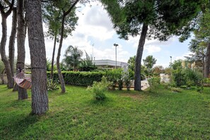 A landscaped garden with trees, a hammock, and a building in the background. - Villa Monti with Private Pool, Wi-Fi, and Air Conditioning (Francavilla Fontana)