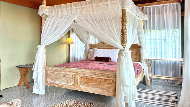 A four-poster bed with a canopy, a small table, and a lamp.