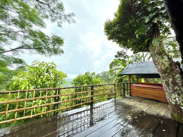 A wooden deck with a bamboo railing overlooking a lush forest.