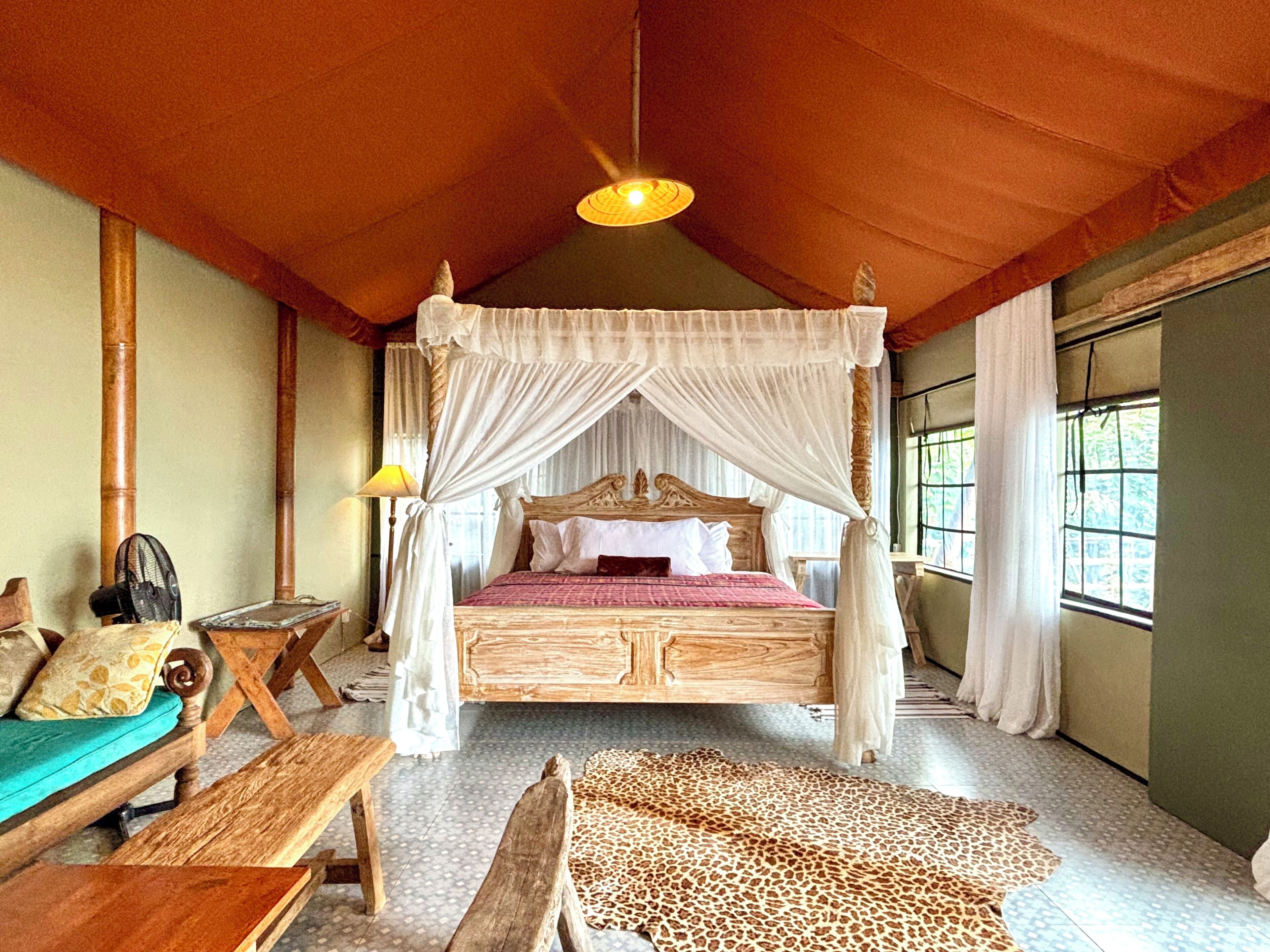 Une chambre avec un lit à baldaquin, un banc en bois, une table et un tapis à motifs léopard.