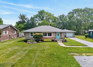 Ein eingeschossiges Haus mit Veranda, Garage und gepflegtem Rasen.