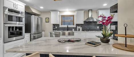 A modern kitchen with built-in appliances, a marble island, and pendant lighting.