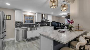 Una cocina moderna con armarios blancos, una isla de mármol e iluminación colgante.