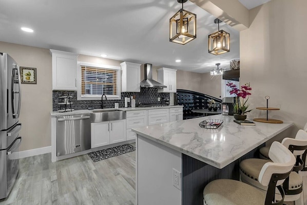 A modern kitchen with white cabinets, a marble island, and pendant lighting.