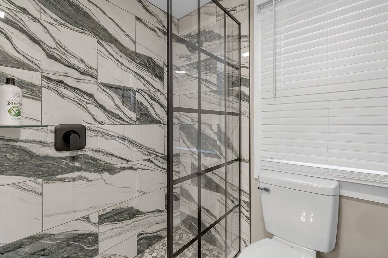 A bathroom with marble tiles, a glass shower enclosure, and a toilet.