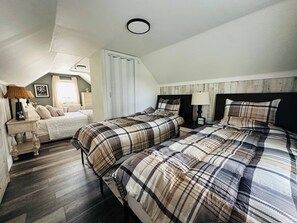 Un dormitorio con dos camas, cabeceras de madera, una mesita de noche con lámpara y una ventana con cortinas.