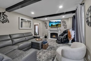 A modern living room with a grey sectional sofa, a fireplace, a mounted TV, and a large abstract wall art piece.