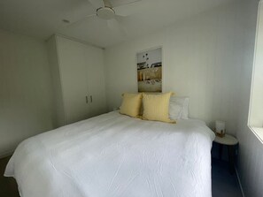 Une chambre à coucher comprenant un lit, une table de chevet, un ventilateur de plafond et un tableau accroché au mur.