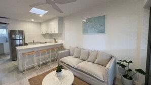 A modern kitchen with a bar area, a white sofa, and a ceiling fan. - Killara Apt 1 - Noosa Heads Holiday Apartment (Noosa Heads)