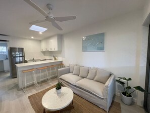 A modern kitchen with a bar area, a white sofa, and a ceiling fan. - Killara Apt 1 - Noosa Heads Holiday Apartment (Noosa Heads)