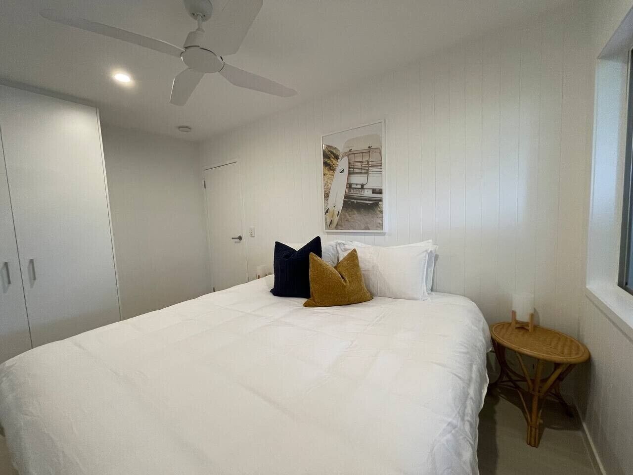 A bedroom with a bed, pillows, a ceiling fan, a window, and a small round table.