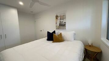 A bedroom with a bed, pillows, a ceiling fan, a window, and a small round table.