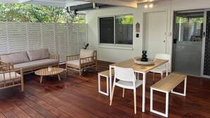 A covered outdoor area with a wooden floor, a sofa, a dining table with chairs, and a sliding glass door. - Killara Apt 1 - Noosa Heads Holiday Apartment (Noosa Heads)