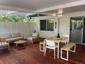 A covered outdoor area with a wooden floor, a sofa, a dining table with chairs, and a sliding glass door. - Killara Apt 1 - Noosa Heads Holiday Apartment (Noosa Heads)