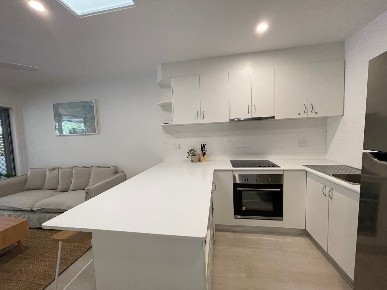 A modern kitchen with white cabinetry, a built-in oven, and a stainless steel refrigerator.