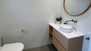 A bathroom with a toilet, a sink with a mirror, and a small plant on the vanity. - Killara Apt 2 - Noosa Heads Holiday Apartment (Noosa Heads)