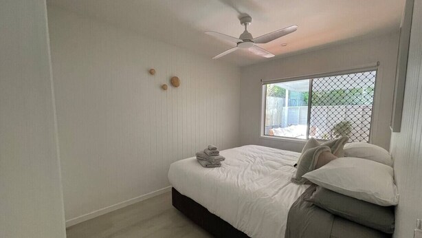 A bedroom with a bed, a ceiling fan, a window with a view, and a bedside table with a lamp. - Killara Apt 4 - Noosa Heads Holiday Apartment (Noosa Heads)