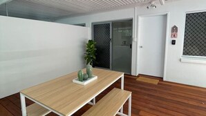 A modern interior with a wooden floor, a white table with benches, a potted plant, and a door with a number plate. - Killara Apt 4 - Noosa Heads Holiday Apartment (Noosa Heads)