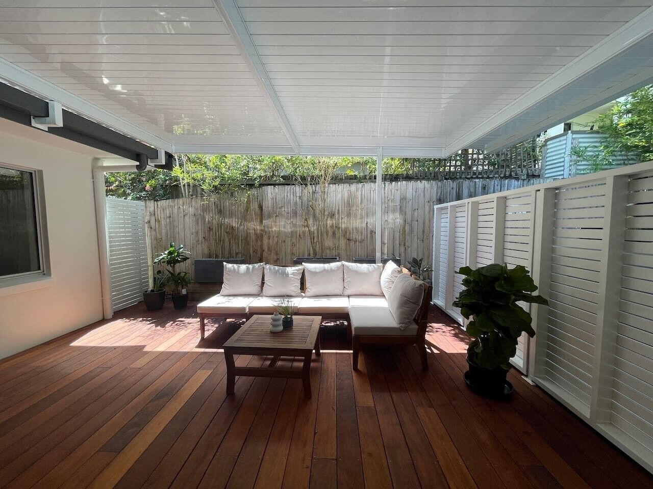 A covered patio with a wooden floor, a white sofa, and a table.