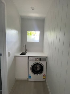 A compact laundry room with a built-in washer and dryer, a small window, and a sink. - Killara Apt 4 - Noosa Heads Holiday Apartment (Noosa Heads)