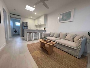 A modern living room with a sofa, coffee table, and a kitchen in the background. - Killara Apt 3 - Noosa Heads Holiday Apartment (Noosa Heads)