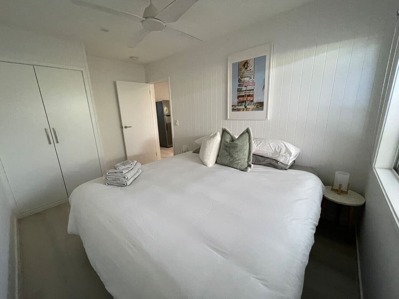 A bedroom with a large bed, a wardrobe, a bedside table with a lamp, and a door leading to another room.
