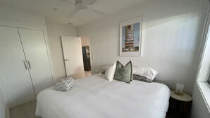 A bedroom with a large bed, a wardrobe, a bedside table with a lamp, and a door leading to another room. - Killara Apt 3 - Noosa Heads Holiday Apartment (Noosa Heads)