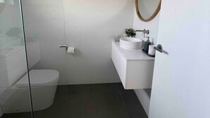A modern bathroom with a glass shower enclosure, a toilet, a sink with a mirror, and a small plant. - Killara Apt 3 - Noosa Heads Holiday Apartment (Noosa Heads)