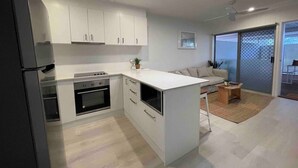 A modern kitchen with white cabinets, a built-in oven, and a dining area with a sofa and coffee table. - Killara Apt 3 - Noosa Heads Holiday Apartment (Noosa Heads)