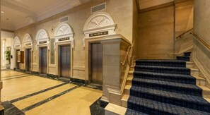 A hotel lobby with marble flooring, a staircase with blue carpet, and multiple elevators. - Down town Industrial Loft w/ Exposed Brick (Houston)