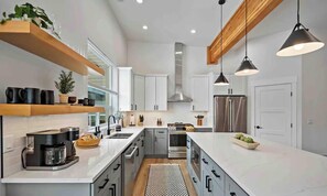 Una cucina moderna con mobili bianchi, una grande isola, elettrodomestici in acciaio inossidabile e illuminazione a sospensione.