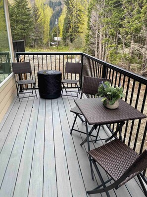 Eine Holzterrasse mit Tisch und Stühlen, umgeben von einem Metallgeländer, mit Blick auf einen bewaldeten Bereich.