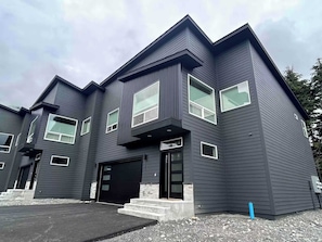 Ein modernes, zweistöckiges Haus mit schwarzem Anstrich, großen Fenstern und einer Garage.