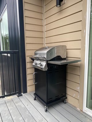 Un barbecue portable doté d’un écran numérique, placé sur une terrasse en bois, devant une maison dont le revêtement extérieur est de couleur beige.