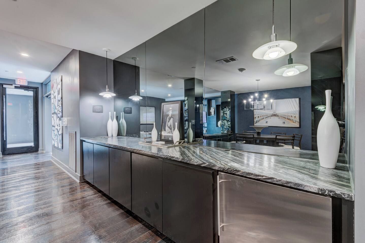 A modern kitchen with a marble countertop, pendant lighting, and a large mirror.