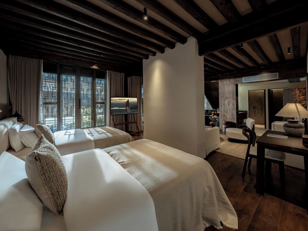 Habitación de hotel con dos camas, zona de estar y vistas a la ciudad.