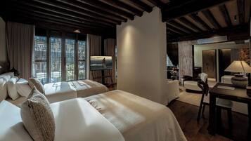 Habitación de hotel con dos camas, zona de estar y vistas a la ciudad.