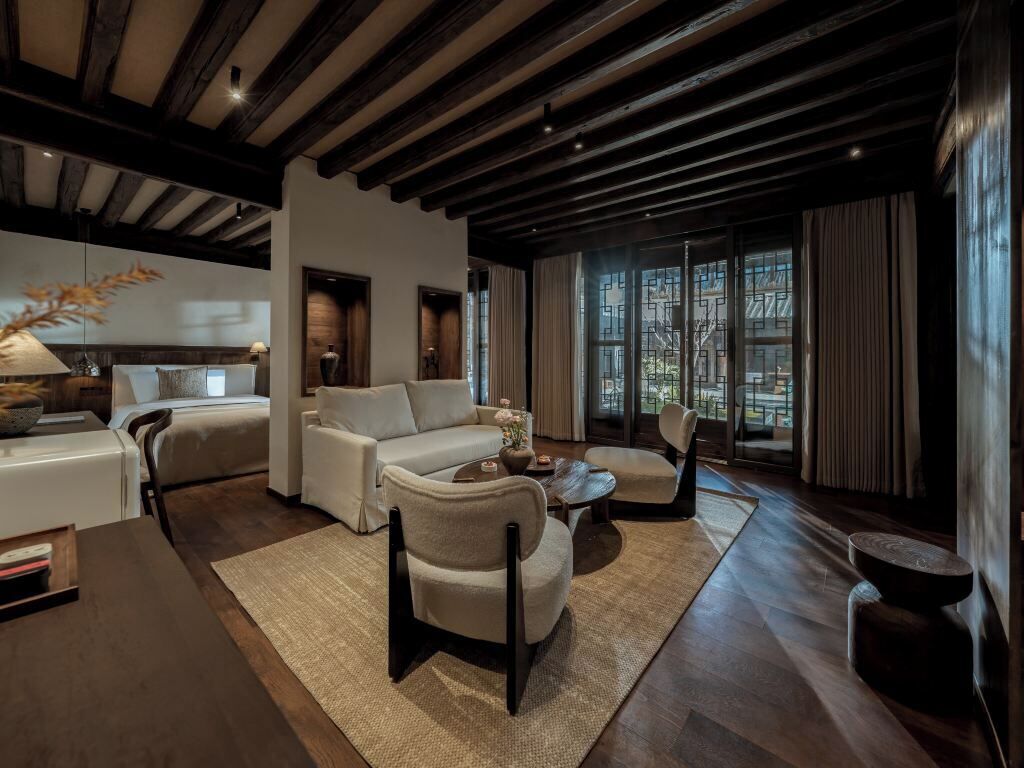 Una sala de estar moderna con sofá, sillones, una mesa de centro y una chimenea. Hay un ventanal con cortinas y vistas al exterior.