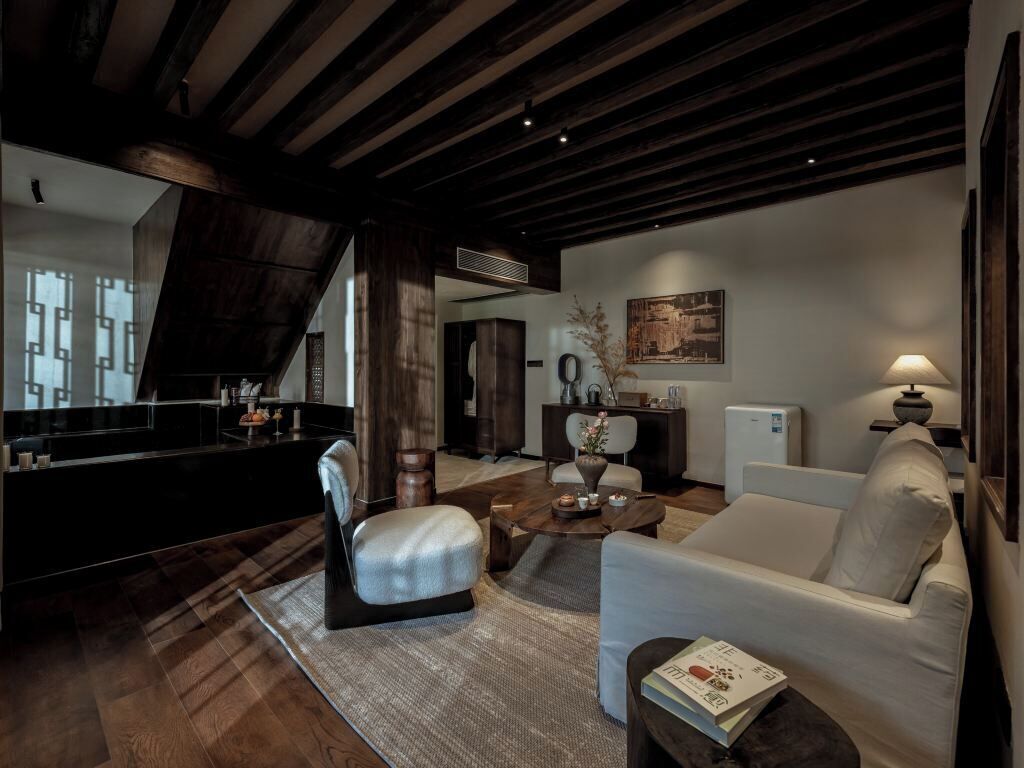 A modern living room with a dark wooden ceiling, a white sofa, a coffee table, and a bookshelf.