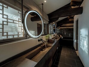 Un baño moderno con un tocador alargado, varios espejos y una ventana con diseño geométrico.
