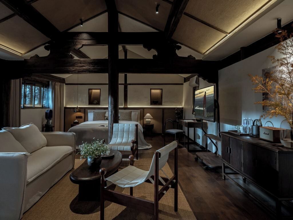 A hotel room with a bed, a sofa, a dining table, and a television.