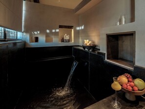 Un baño moderno con una bañera negra, un pequeño elemento decorativo tipo cascada y un frutero sobre el mostrador.