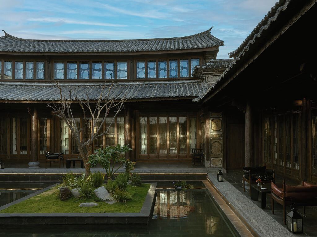 Un edificio tradicional con un patio, un estanque y mobiliario de madera.