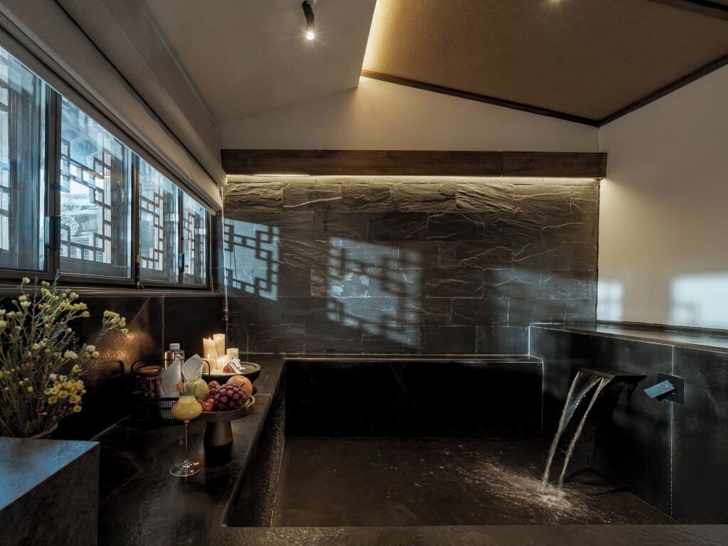 A modern bathroom with a stone wall, a bathtub, and a window with a view.