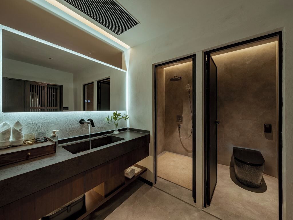 Un baño moderno con un espejo grande, lavamanos dobles, zona de ducha y un inodoro.