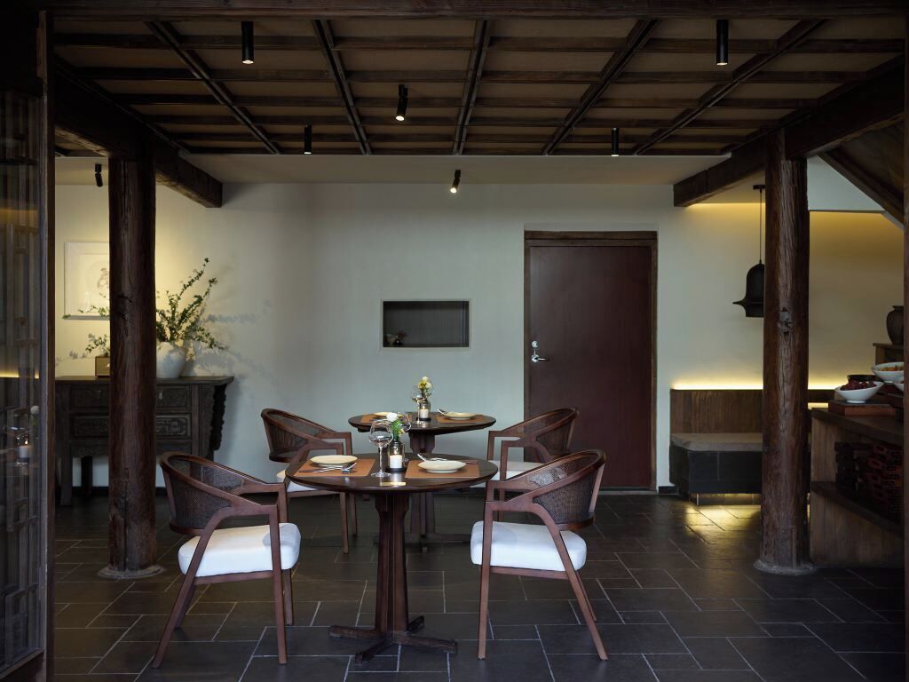 Uma sala de jantar com uma mesa redonda, quatro cadeiras e teto de madeira escura.