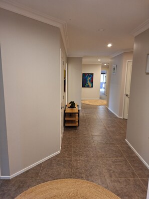 A hallway with a wooden bench, a rug, and a painting on the wall. - Sunny Coastal Escape with Pool and Stunning Ocean Views! (Whangarei)