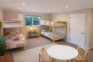 Een kamer met stapelbedden, een klein tafeltje met stoelen, een kamerplant en een raam met natuurlijk licht.