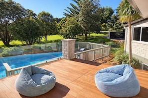A deck with a pool, two bean bags, and a stone pillar. - Sunny Coastal Escape with Pool and Stunning Ocean Views! (Whangarei)