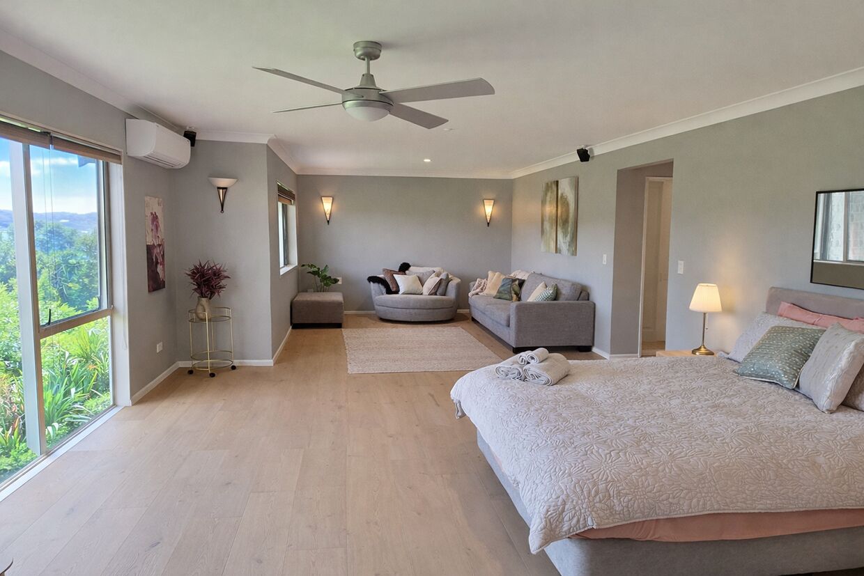 Un dormitorio con una cama grande, ventilador de techo, zona de estar y vistas amplias por una ventana.